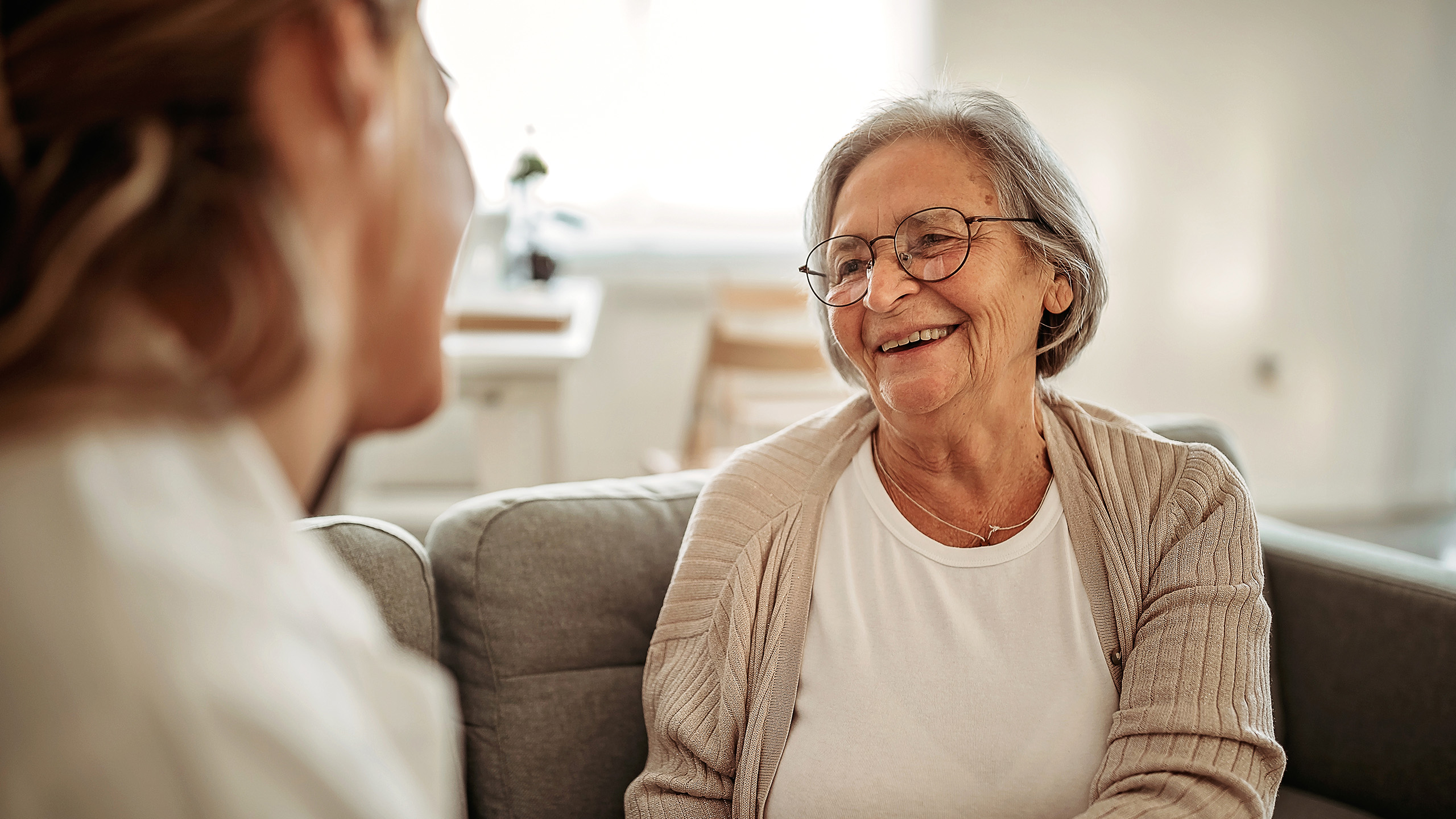 Senior woman sitting on sofa speaking to young woman.