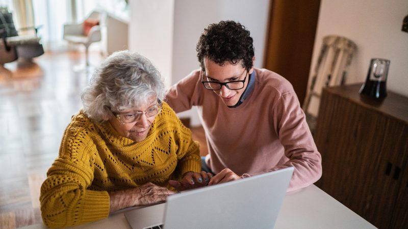 Young man helping senior woman on laptop at home.